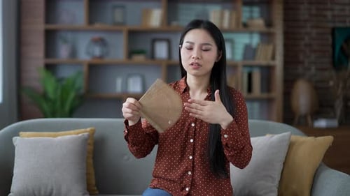 Young adult asian woman is hot while sitting on the sofa in living room at home. Displeased female