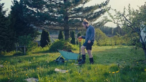 Man With A Wheelbarrow In A Green Garden - Wide Shot