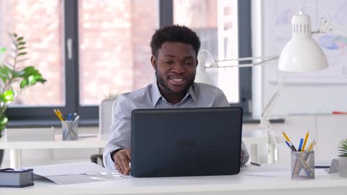 Happy african american businessman enjoys video chat on laptop at modern office