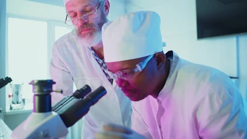 Scientists Studying Sample Through Microscope in Lab