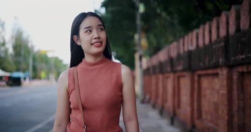 A young Asian woman is walking happily on the sidewalk.