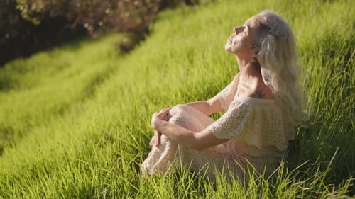 Serene Senior Woman Embraces Nature Tranquility in Green Grass Golden Sunlight and Fresh Air