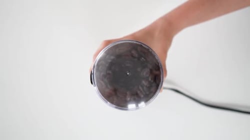 Top down view of person hand grounding coffee beans in electric grinder