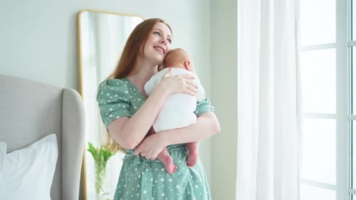 Mother Holding Newborn Baby in Sunny Bedroom