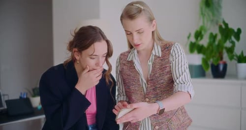Two Young Adults Looking at Phone Together Indoors