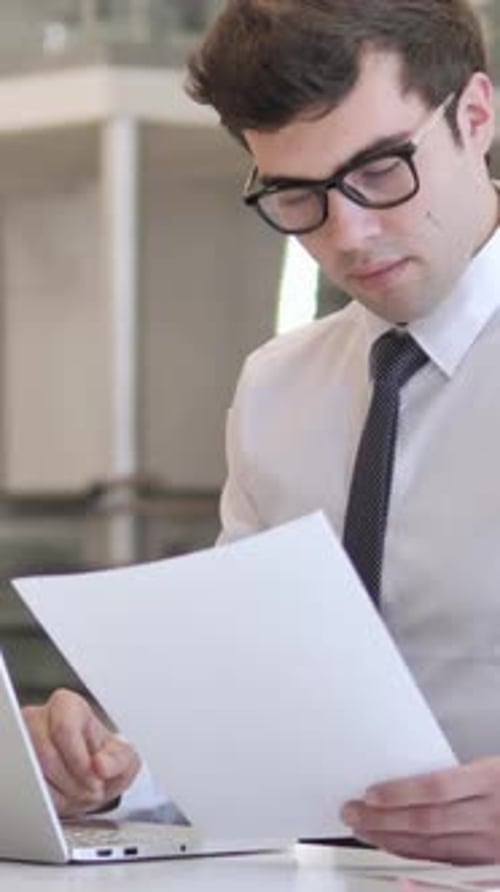 Man in Shirt Reading Reports at Desk