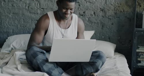 Man Using Laptop and Laughing in Bed