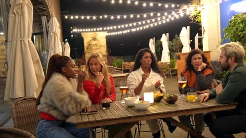 Multiethnic Friends Sitting on a Bar Terrace Drinking at Night