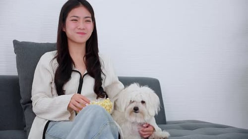 Woman Eating Popcorn on Couch with White Dog