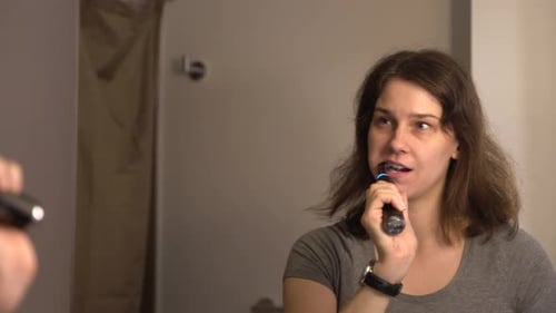 Mujer joven cepillándose los dientes en el baño 4K