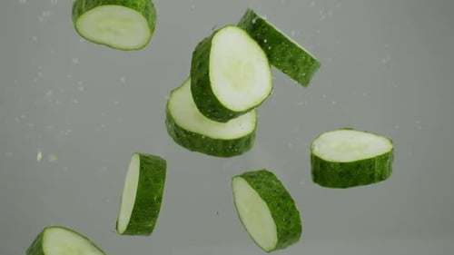 Green cucumber falling into transparent water on white grey background