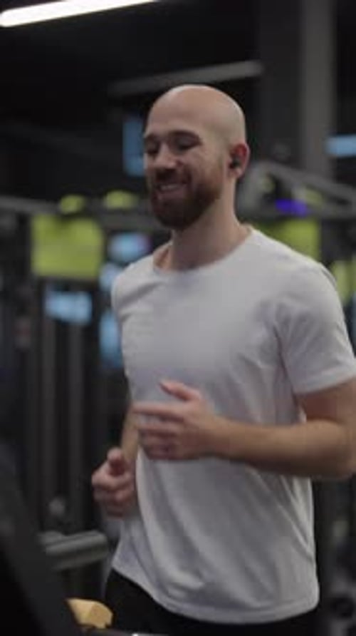 Bald Man Runs On Treadmill In Gym Wearing Earbuds