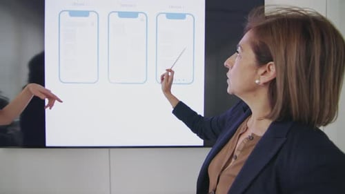 dos mujeres profesionales en una reunión de negocios, una de las cuales señala los diseños de estructuras alámbricas que se exhiben