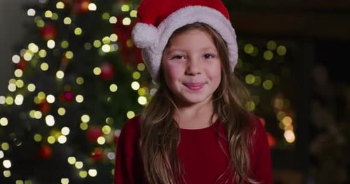 Smiling Girl in Santa Hat Near Christmas Tree