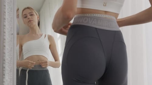 Young Woman Measures Waist in Mirror at Home