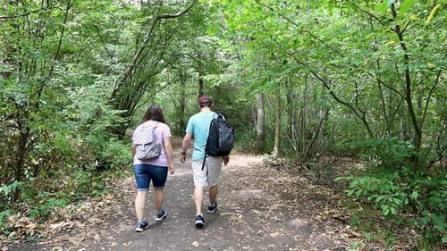 Couple walking on the path in the forest and exploring nature. Man and woman with backpacks hiking i