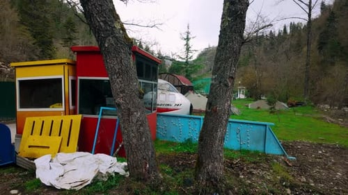 Yellow and red booths, blue barrier, and airplane fuselage with tents framed by trees in Borjomi,...