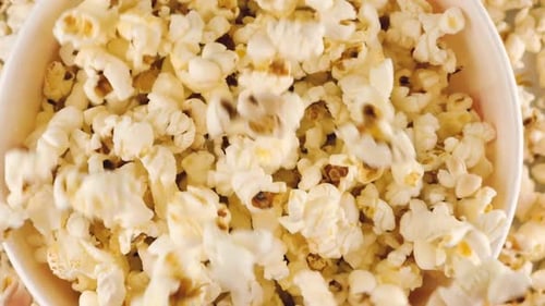 Grains de pop-corn tombant dans un seau à rayures rouges et blanches isolés sur fond blanc.