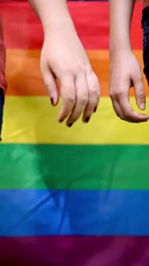 Vidéo en gros plan au ralenti d'un couple de lesbiennes se tenant la main avec un drapeau de fierté arc-en-ciel vibrant