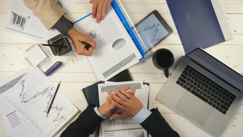 Male Hands of Two Successful Business Partners Examining Graphs and Discussing Financial Reports in