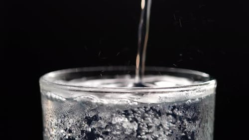 Verter agua con gas en un vaso sobre fondo negro