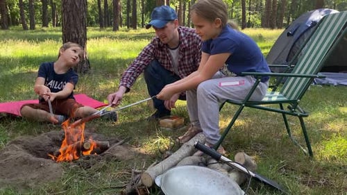 Family Roasting Sausages Over Campfire in Forest