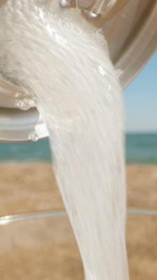 Soda is poured from a can into a glass. The sea is in the background. Summer, sunny day, beach.