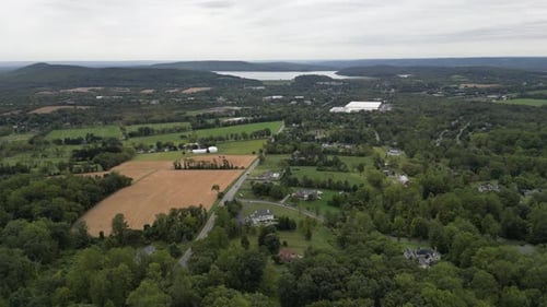 Aerial view flying over a vast rural area featuring lush green forests, harvested farm fields, a