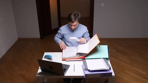 Office Worker Examining Documents with Magnifying Glass at Desk