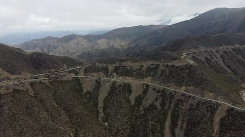 Aerial: Serpentine dirt road winds down mountain pass in switchbacks