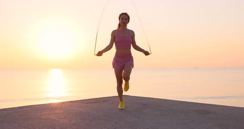 Fit woman jumping rope at the beach during summer vacation. Slow motion
