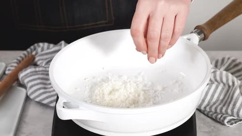 Schritt für Schritt Kokosflocken in einer weißen Antihaftpfanne rösten