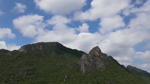 Lovely cotton-like clouds and the mountain with rock tower jutting out while this aerial footage sli