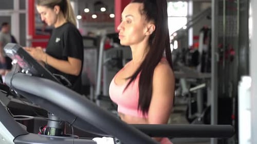 Beautiful Young Woman with a Slim Athletic Figure Running on a Treadmill in a Modern Gym