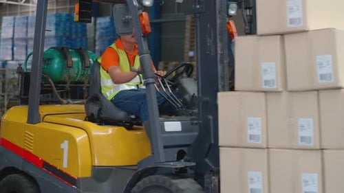 Warehouse worker drive folklift car carry stack of product carton then stop and look at camera