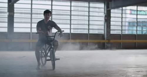 Sportsman Sitting on BMX in Parking Lot with Smoke During Training