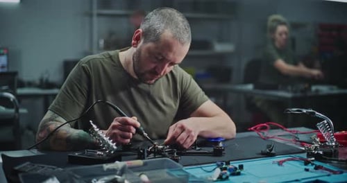 Arbeiter mit Tattoo am Arm lötet interne Elektronik auf modernen Drohnenrahmen