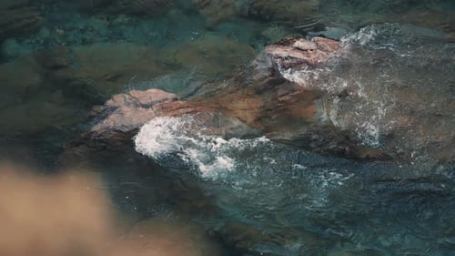 A close-up view of the river. Transparent water flowing swiftly whirling over the stones. Blurry for