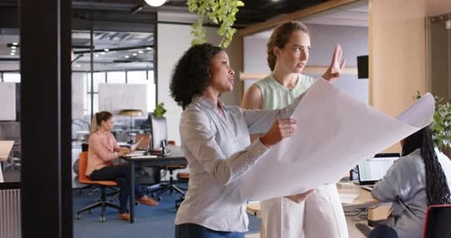 Diverse female architects discussing work and looking at blueprints at office, in slow motion