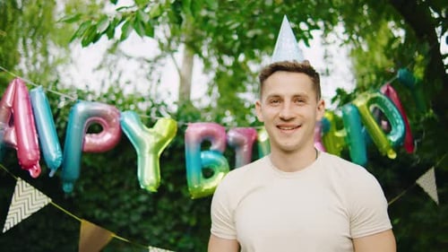 A Cheerful Young Man in a Colorful Party Hat Celebrates His Birthday with Friends and Family in a