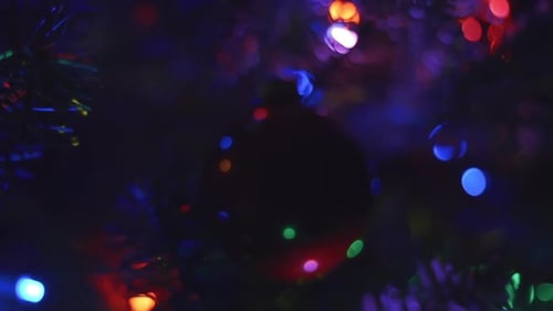 Panning and zooming away from dark, plain, red Christmas tree ornament hanging motionless while mult