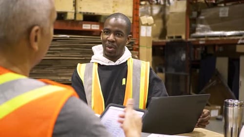 Warehouse supervisors discussing logistics with tablet and laptop technology