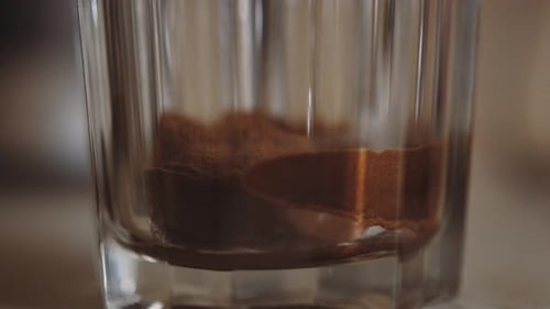 Instant powdered coffee watered in transparent glass, shallow focus close-up, slowmo