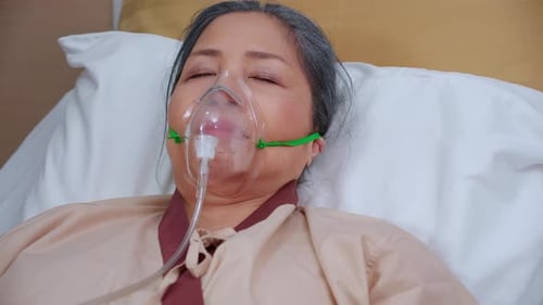 Patient elderly asleep with disease or unconscious in oxygen mask on bed at hospital.