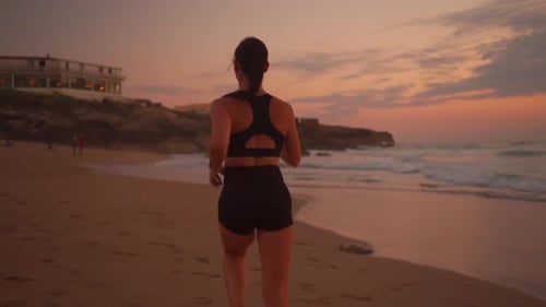 Athletic Woman with Waving Hair Running on Beach at Dramatic Sun Background