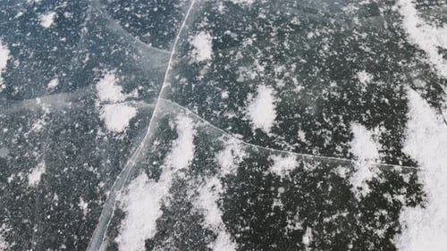 A frozen lake with a layer of ice partially covered by snow. The dark blue surface contrasts