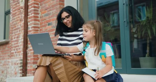 Woman and Child Use Laptop on Building Steps