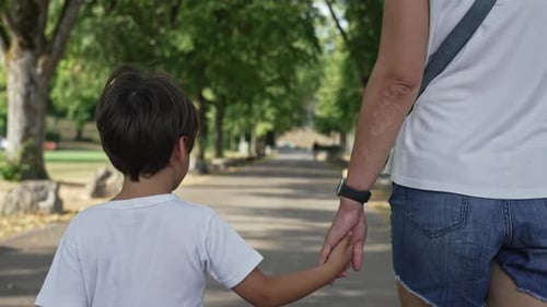 Creando recuerdos duraderos: madre e hijo juntos caminando de la mano por un parque arbolado