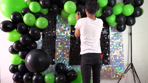 Event decorator aligning green and black balloons for setting backdrop at event