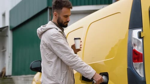Man Disconnecting Electric Vehicle Plug While Holding Coffee